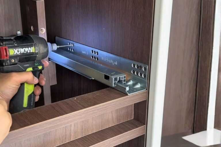 Bottom Drawer Slides: Types, Measurements, and Buying Guide 25 Hand installing a metal drawer slide inside a dark wood cabinet with a cordless drill