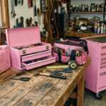 Pink toolboxes and a tool bag on a workbench in a workshop with hand tools and shelves of supplies
