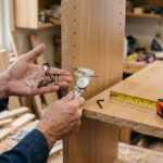 Carpenter measuring a wood panel with calipers, screws, and tape measure in a workshop